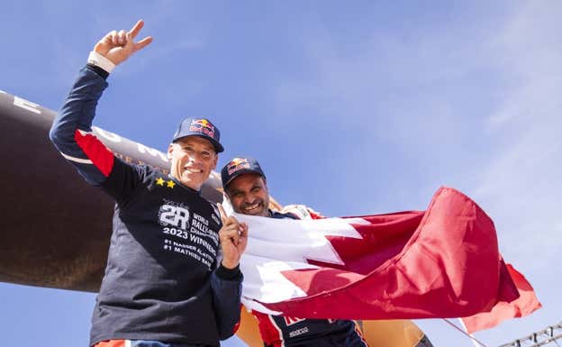 Mathieu Baumel y Nasser Al Attiyah tras proclamarse bicampeones del mundo de rally raid, con la bandera de Catar.  A.S.O/DPPI/J.Delfosse