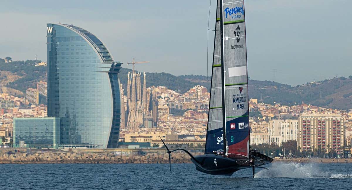 El American Magic navega en Barcelona con el hotel Vela y la Sagrada Familia al fondo.