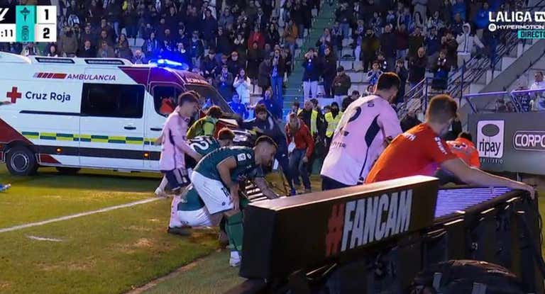 Los jugadores retiran la valla de publicidad para el paso de la ambulancia.